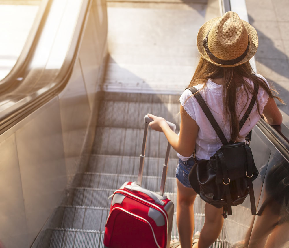 Young,Girl,With,Suitcase,Down,The,Escalator.